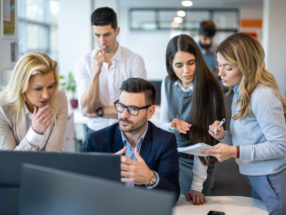 Business people gathered around colleague thoughtfully reviewing business plan and company future decisions