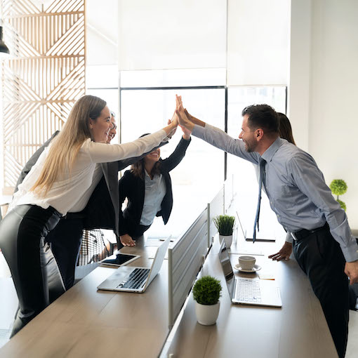 Business people standing around coworking desk in office and giving high five to each other
